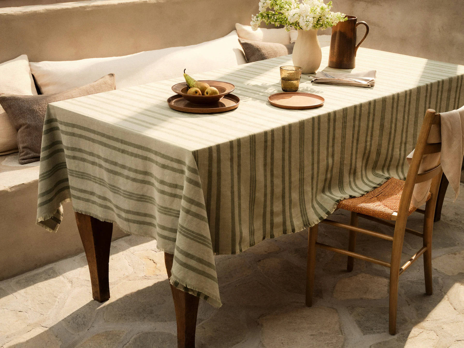 Mesa con mantel lino y asiento de obra con cojines, de Zara Home. 