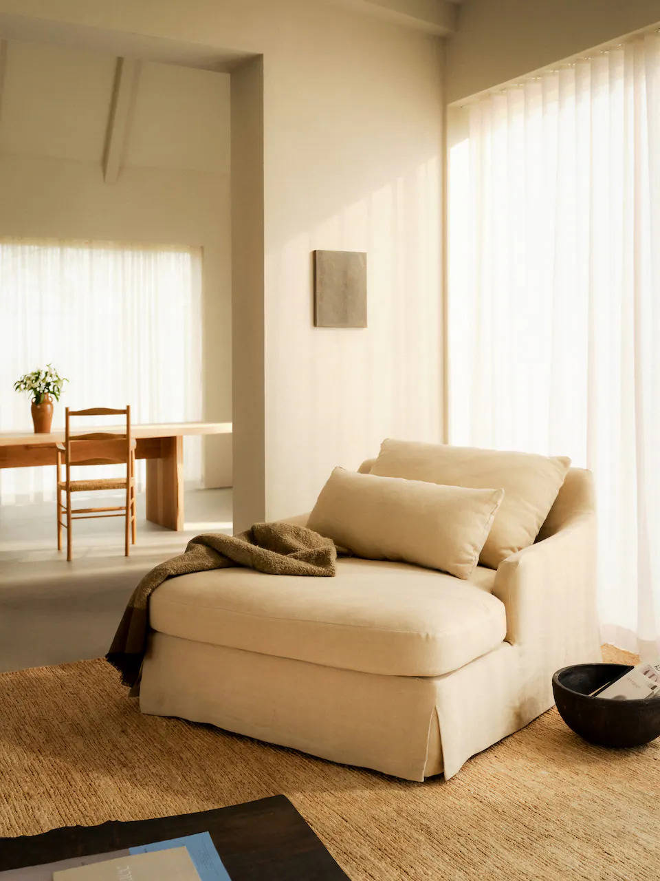 Sofá de dos plazas tapizado en lino natural con manta de lino y alfombra de yute, todo en Zara Home. 