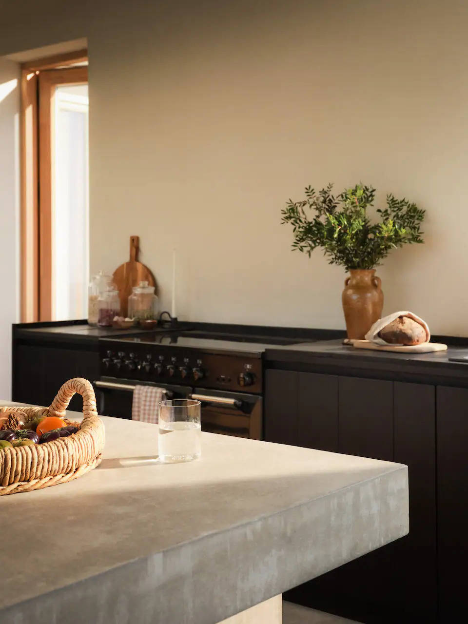 Cocina con mobiliario oscuro e isla con encimera de cemento pulido, de Zara Home. 