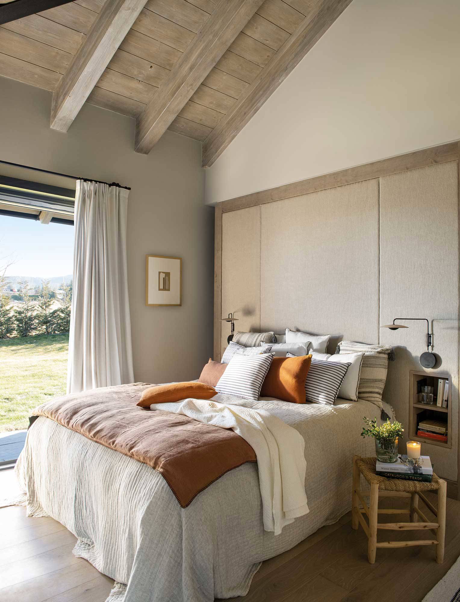 Dormitorio con vigas de madera y gran cabecero tapizado.