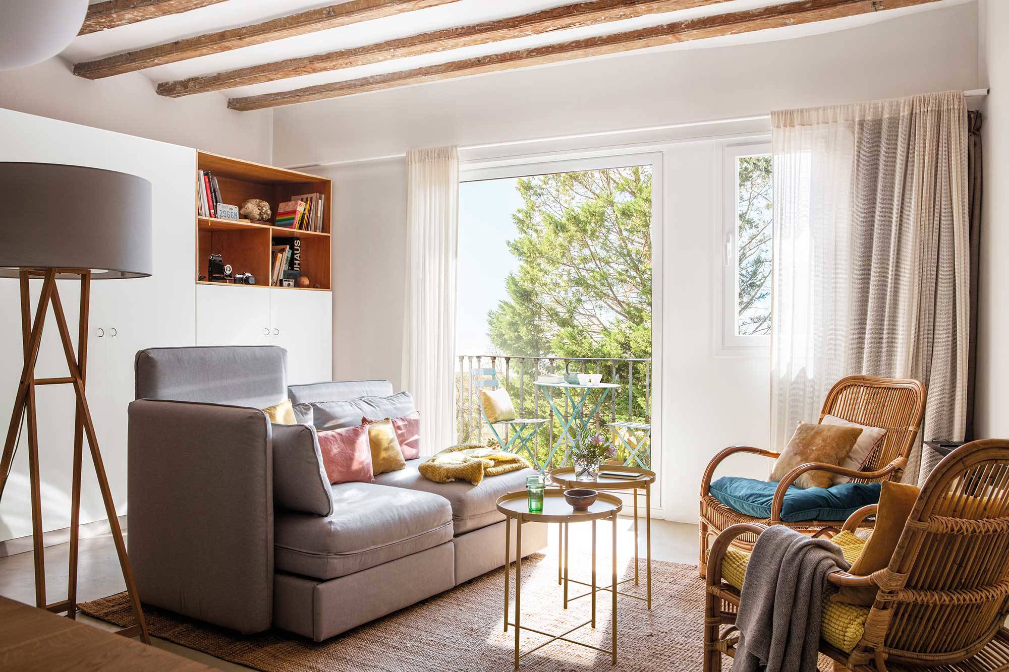 Salón pequeño con sofá gris, butacas, mesas de centro tipo nido y ventana con balcón. 