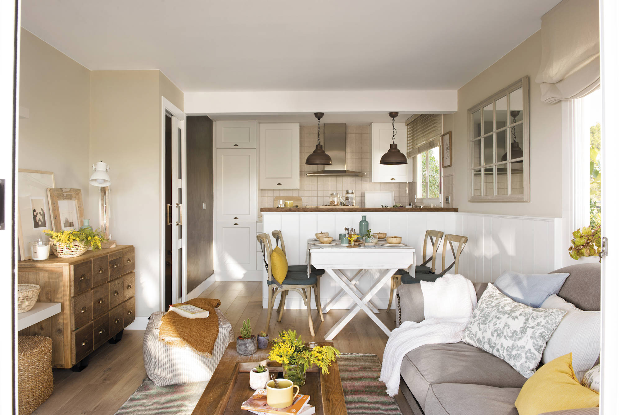 Salón pequeño abierto al comedor y cocina con sofá gris, mesa de centro y cómoda de madera. 