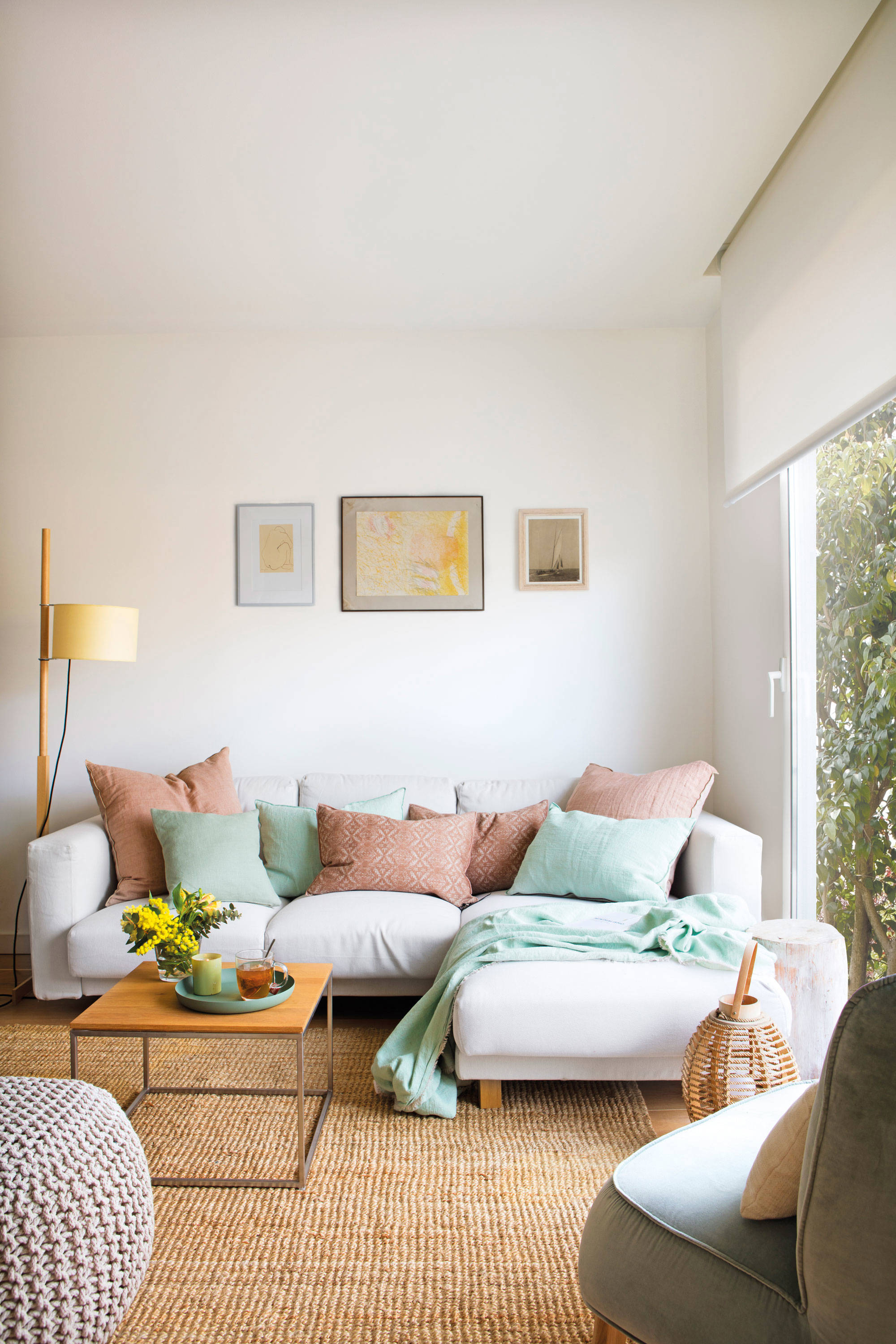 Salón pequeño con sofá en L gris, ventanal y alfombra de fibras.