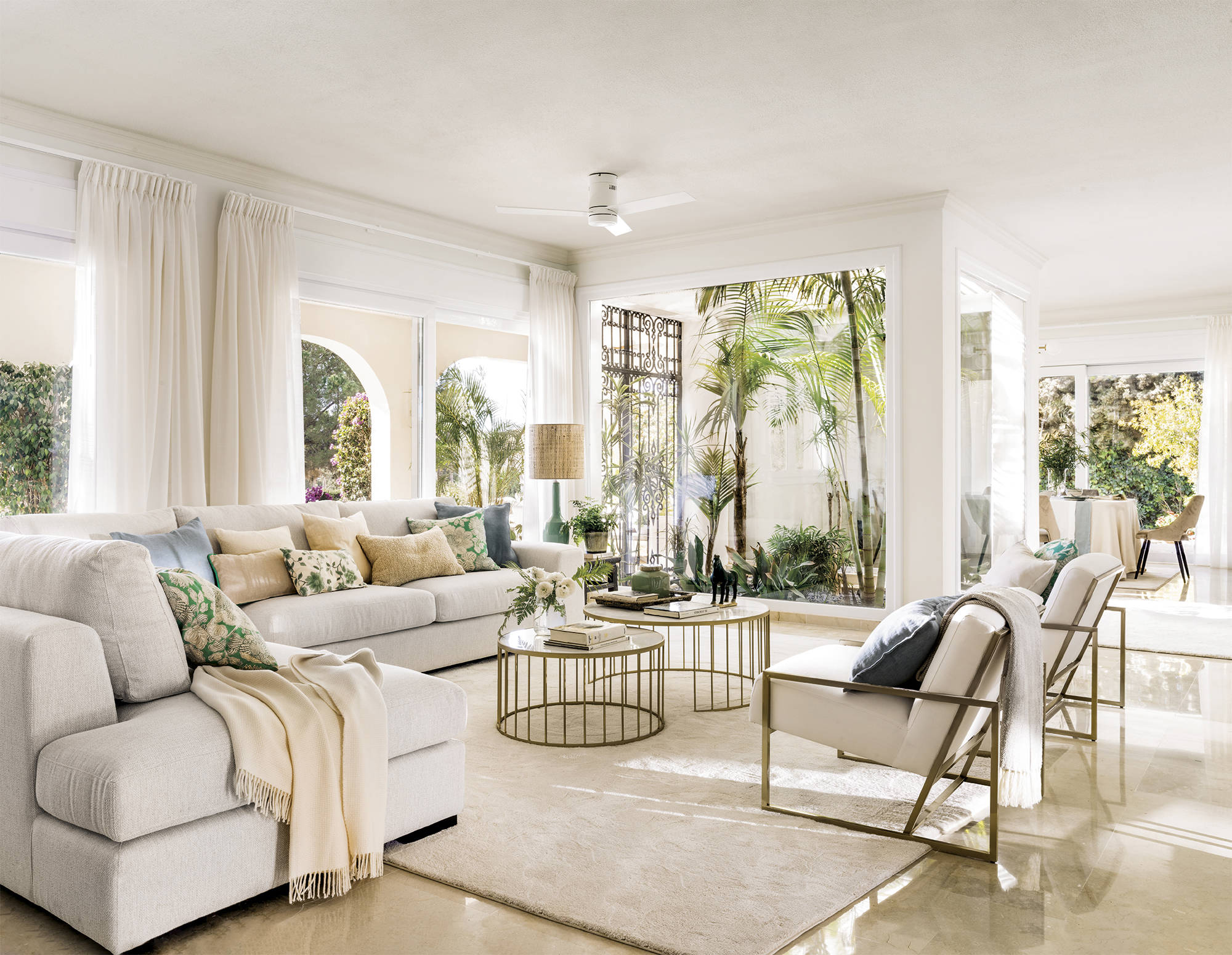 Salón blanco elegante con sofá rinconera, detalles dorados y patio interior