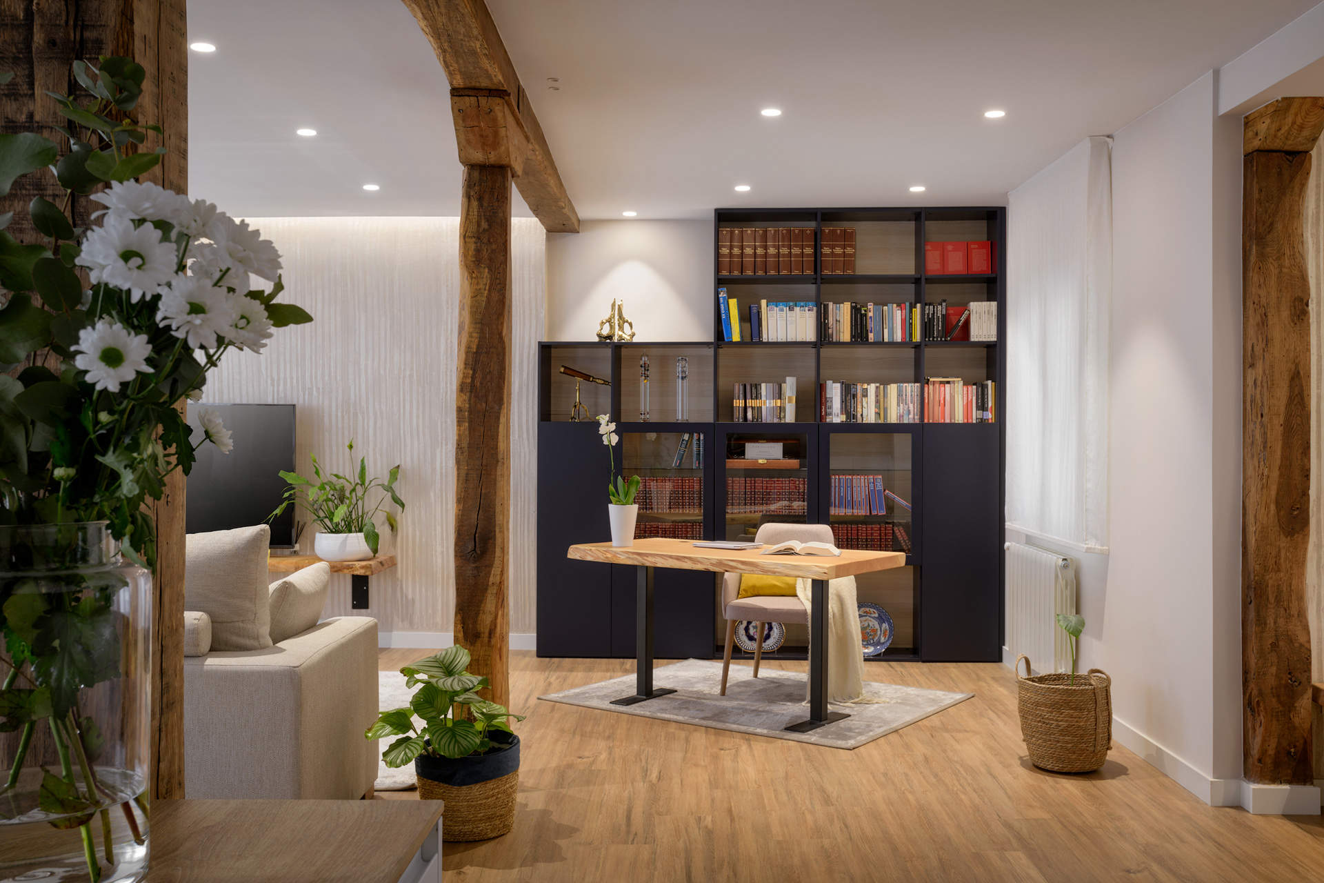 Zona de biblioteca y despacho con mesa de madera, silla, librería negra y alfombra. 