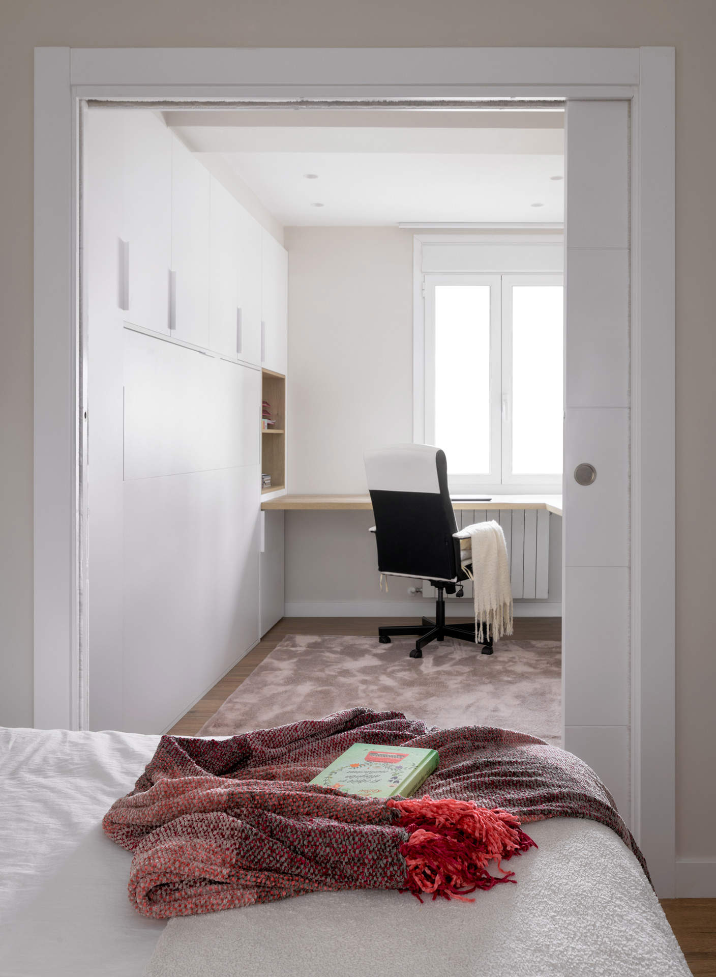 Dormitorio juvenil con alfombra, escritorio frente a la ventana y armario blanco hecho a medida.