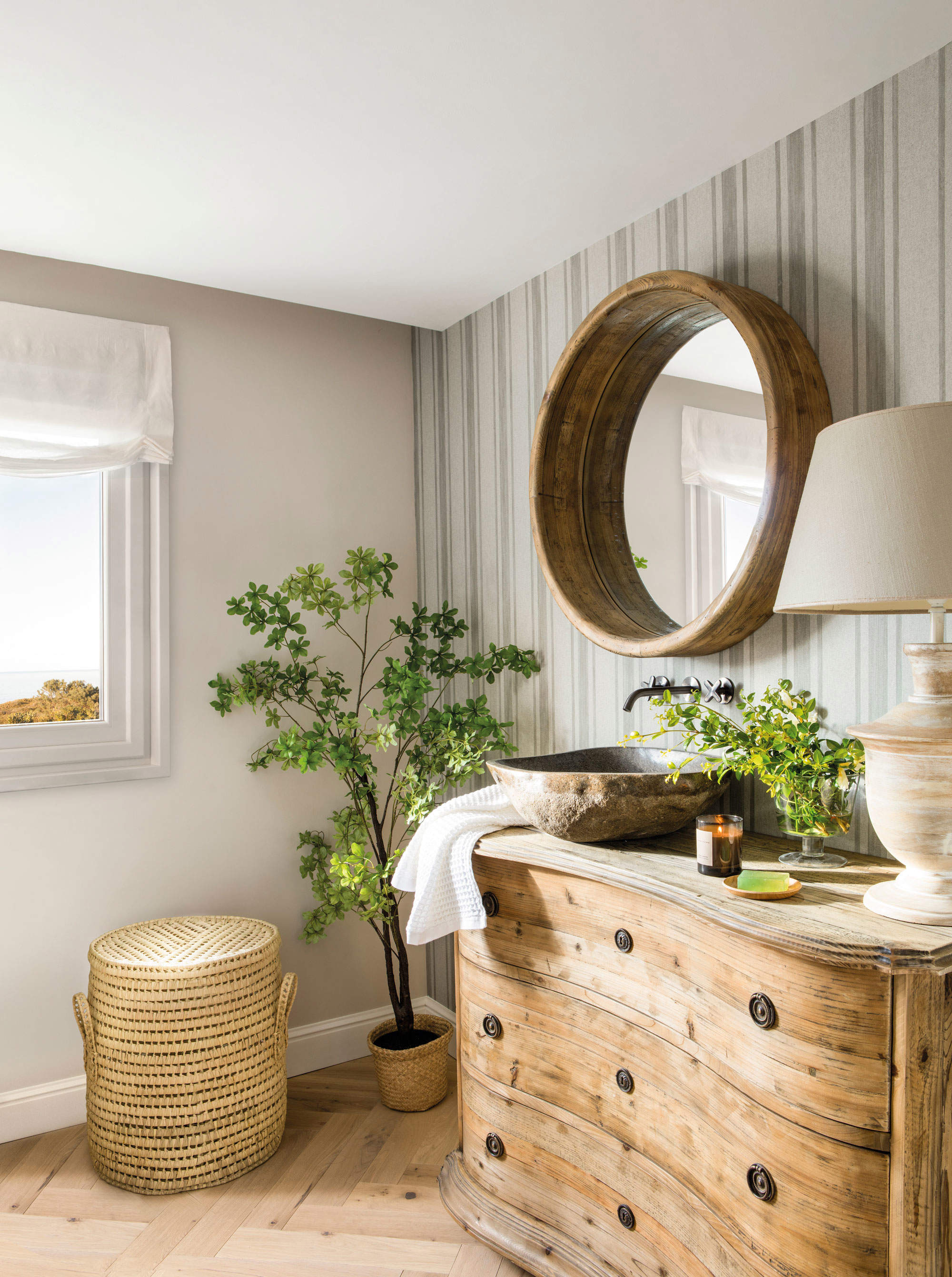 Baño de estilo rústico con una cómoda de madera y un espejo redondo.