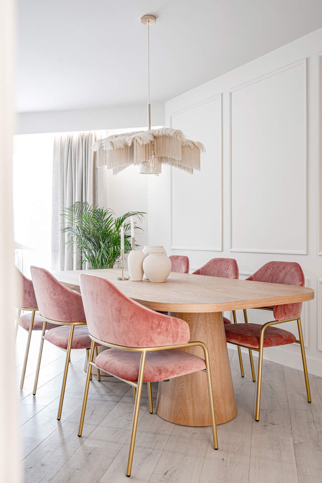 Comedor después de la reforma con sillas tapizadas rosas, molduras en la pared, mesa de madera y brazos en metal dorado..