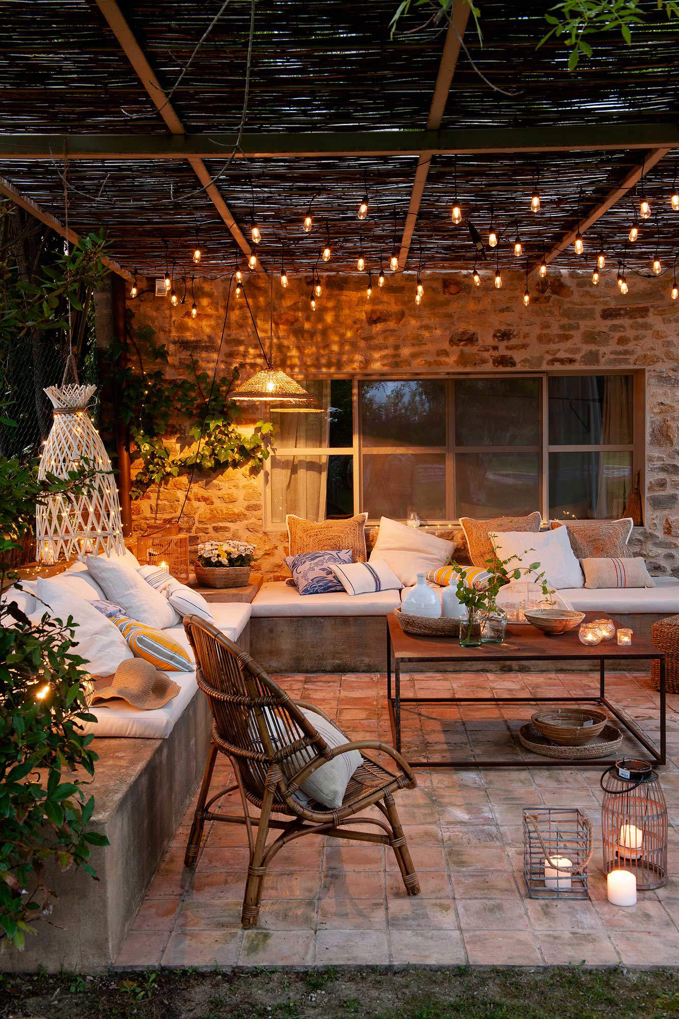 Terraza con sofá en L, pérgola de cañizo, guirnaldas de luces y velas.
