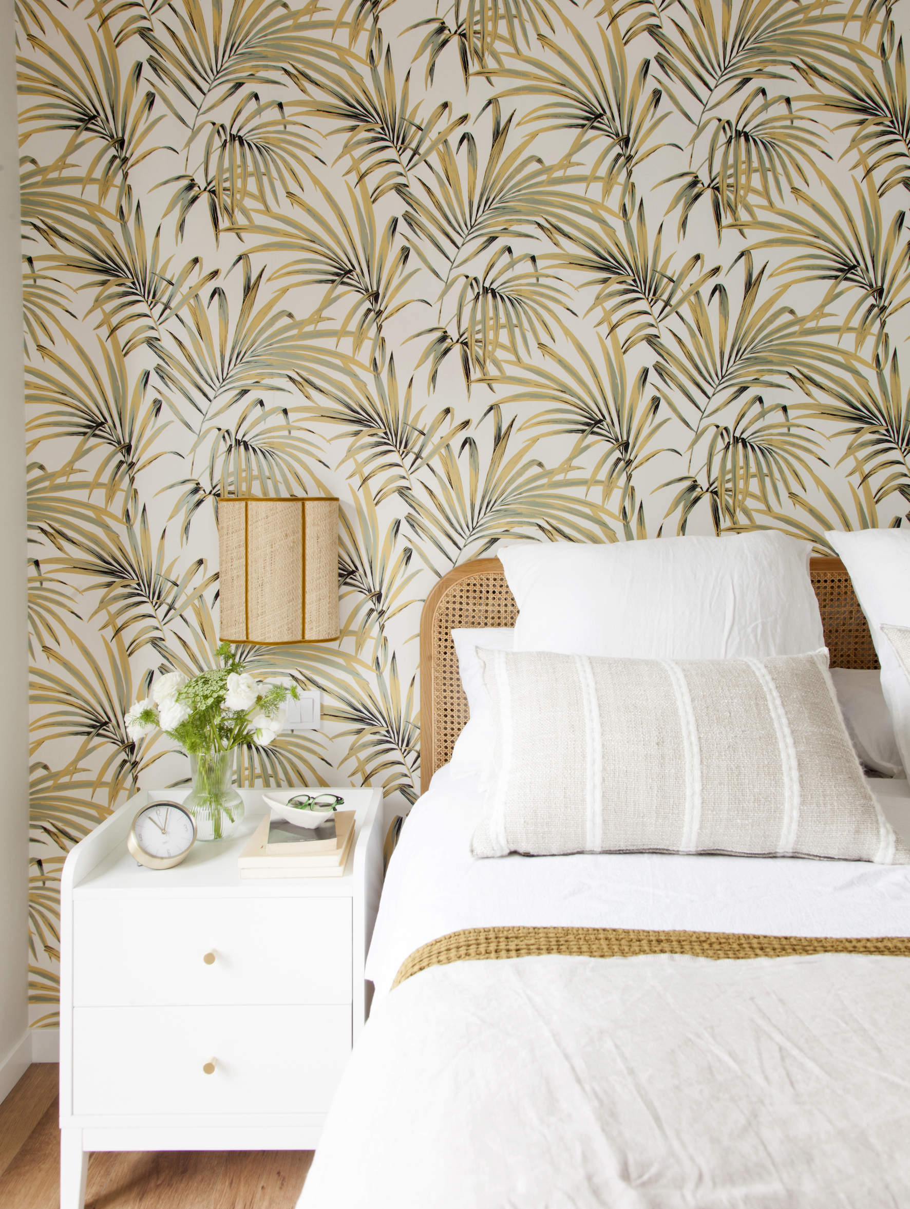 Dormitorio con papel pintado de hojas, cabecero de fibras y mesita blanca Majo Flores