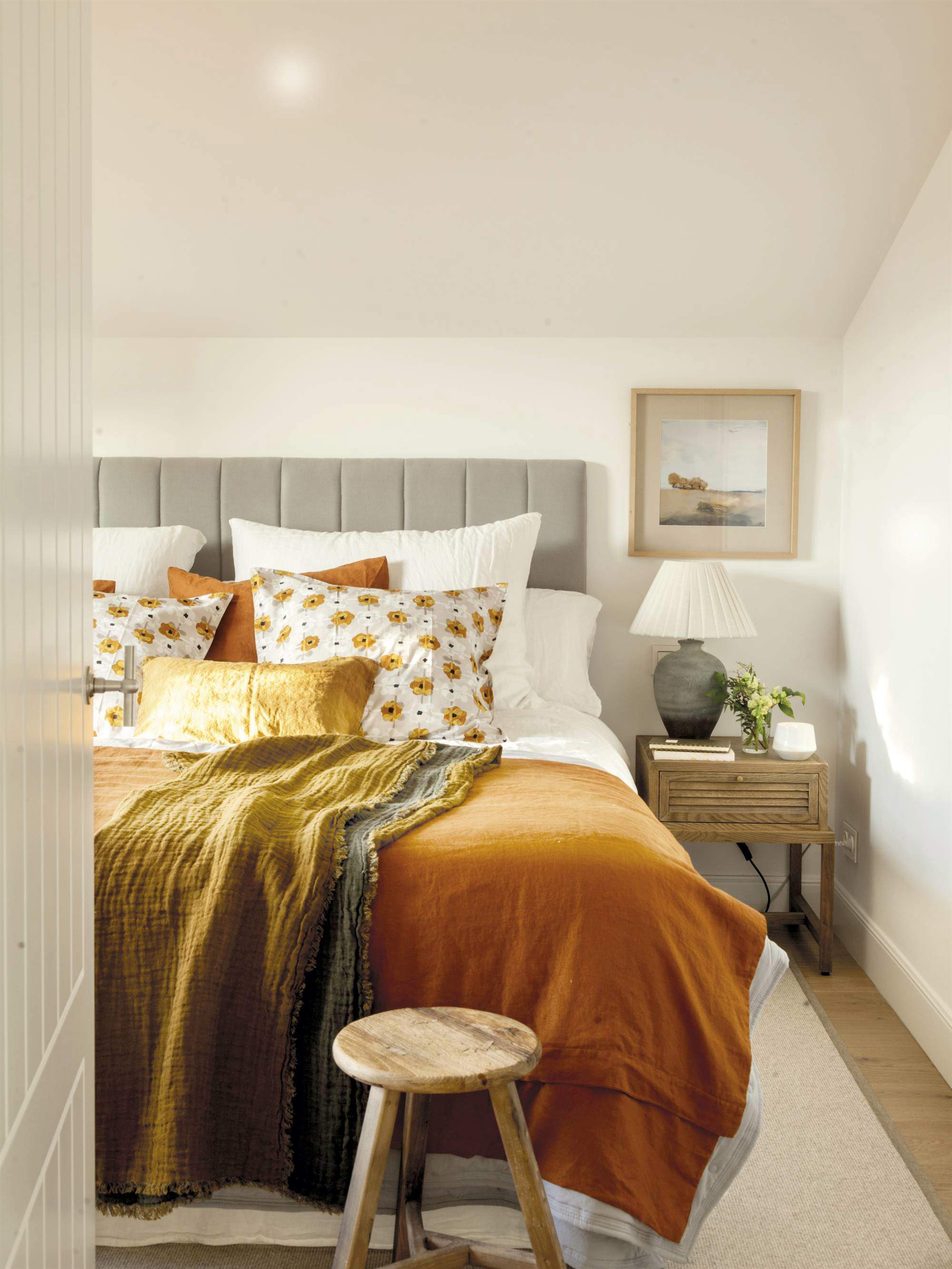 Dormitorio blanco con cabecero gris y ropa de cama en tonos ocres.