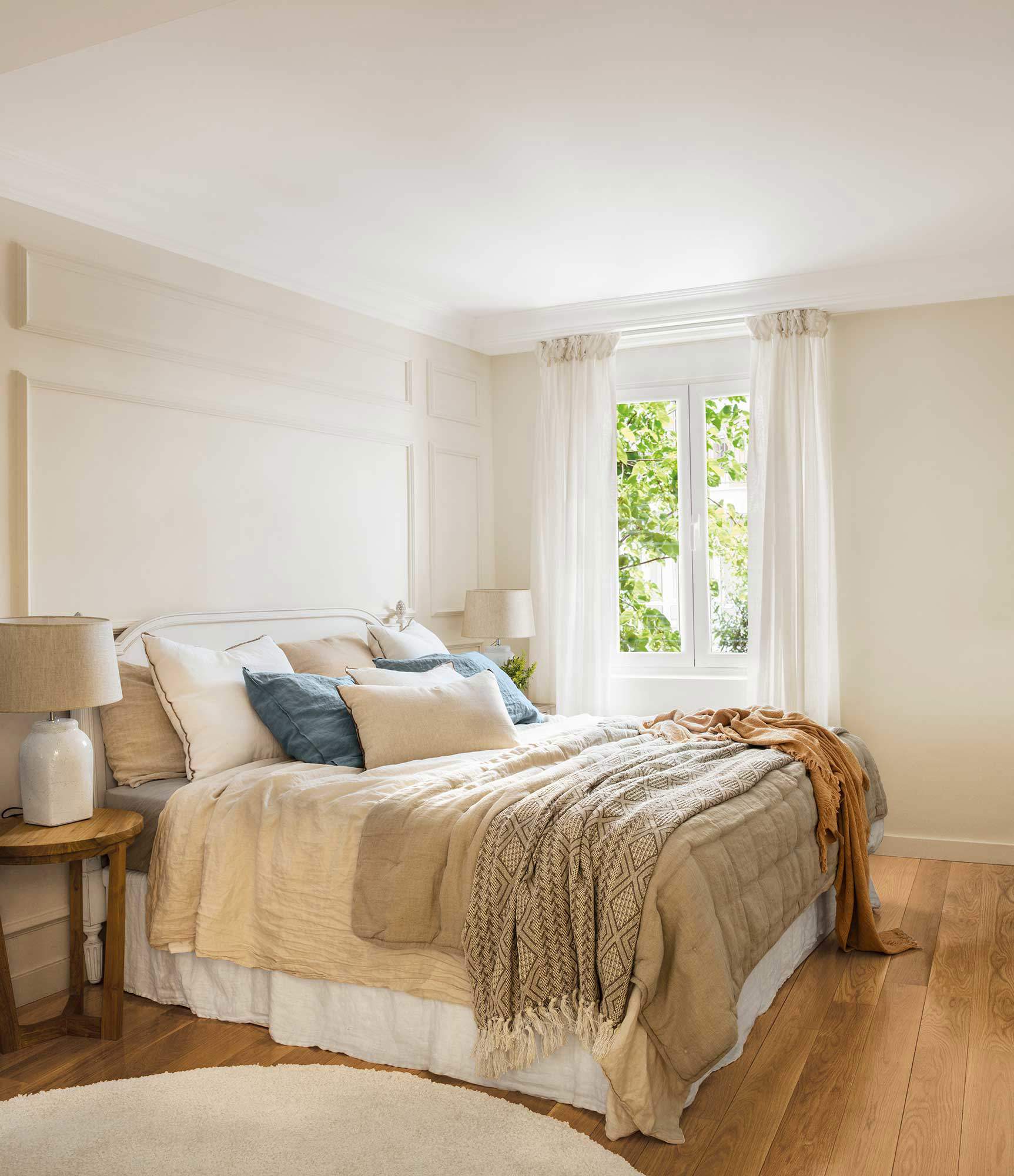 Dormitorio con cabecero blanco y mesitas de madera. 