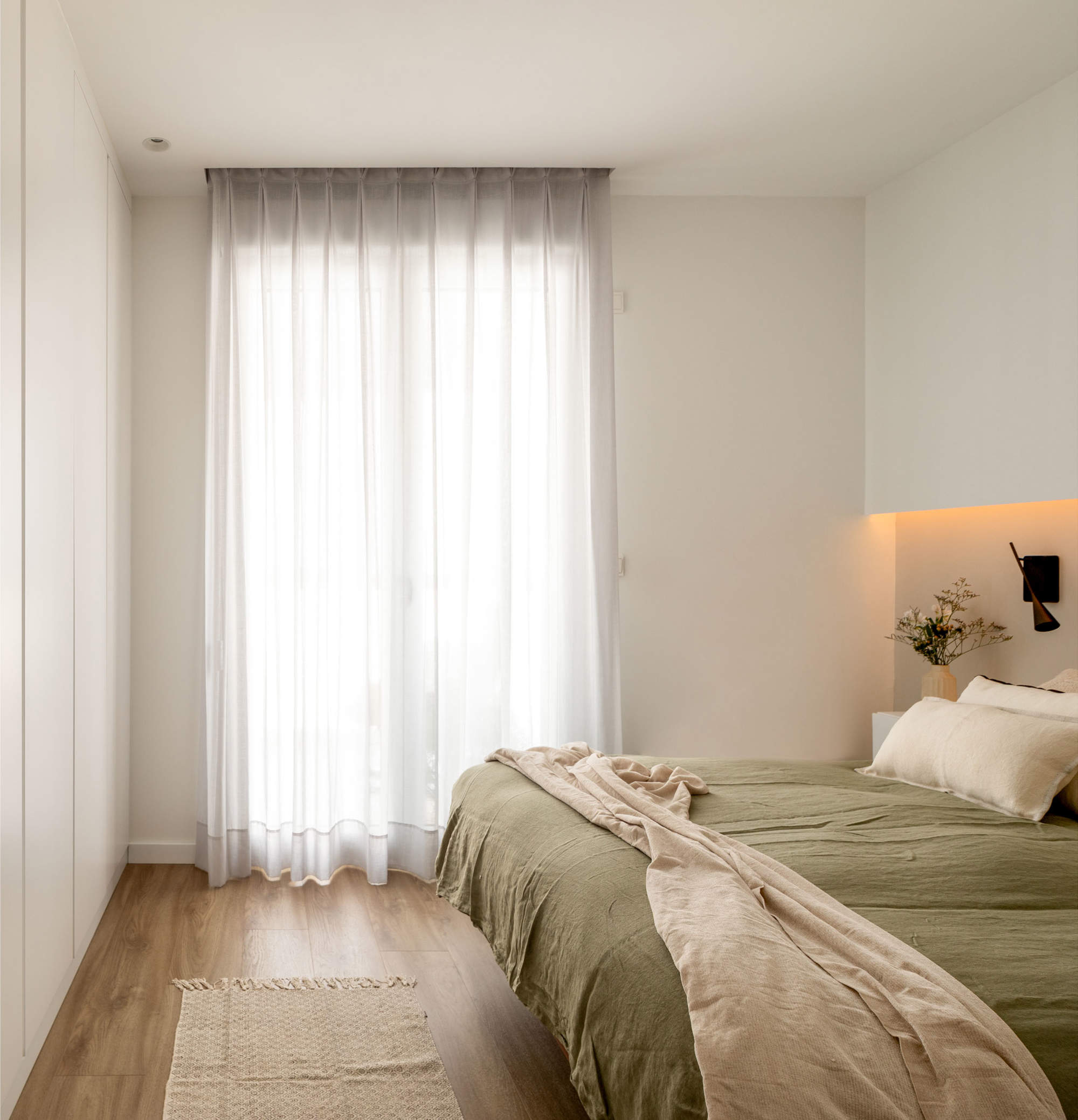 Dormitorio después de la reforma con cortinas, cama verde y armario empotrado lacado en blanco.