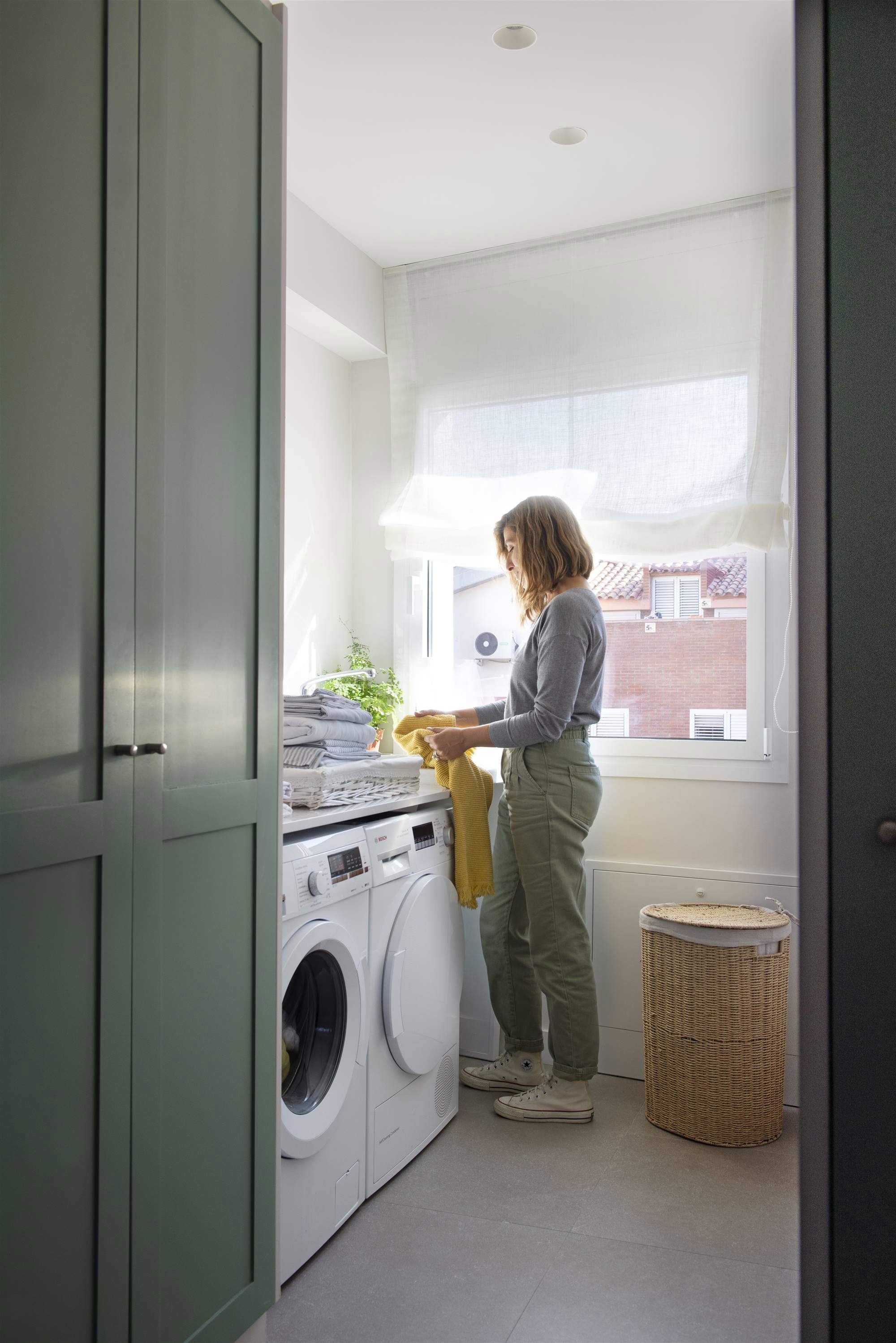 Mujer recogiendo ropa de la colada junto a una lavadora.