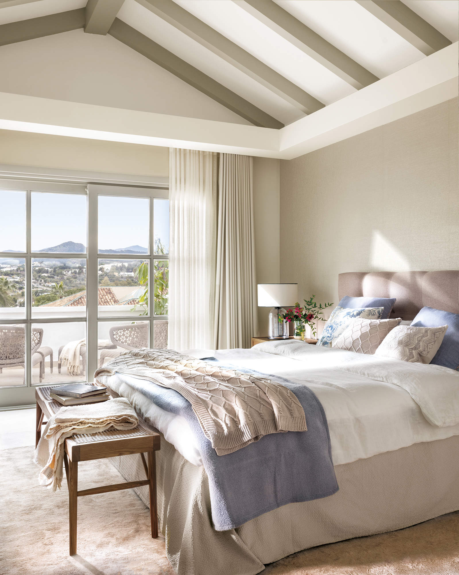 dormitorio principal con salida a terraza privada, ropa de cama beige y azul, cabecero tapizado, banqueta con rejilla, alfombra beige, 