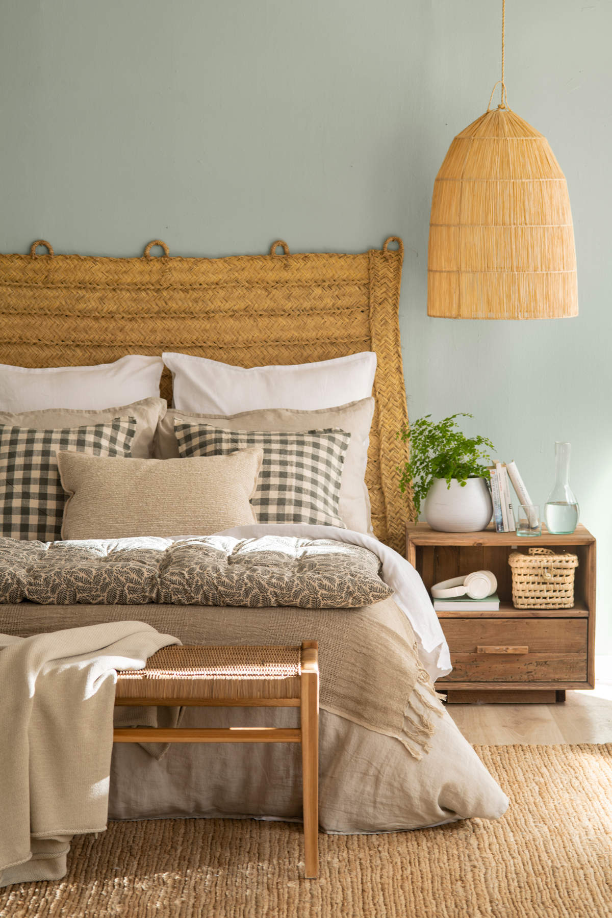 Un dormitorio con cabecero, lámpara, cestas y alfombra de fibra natural.