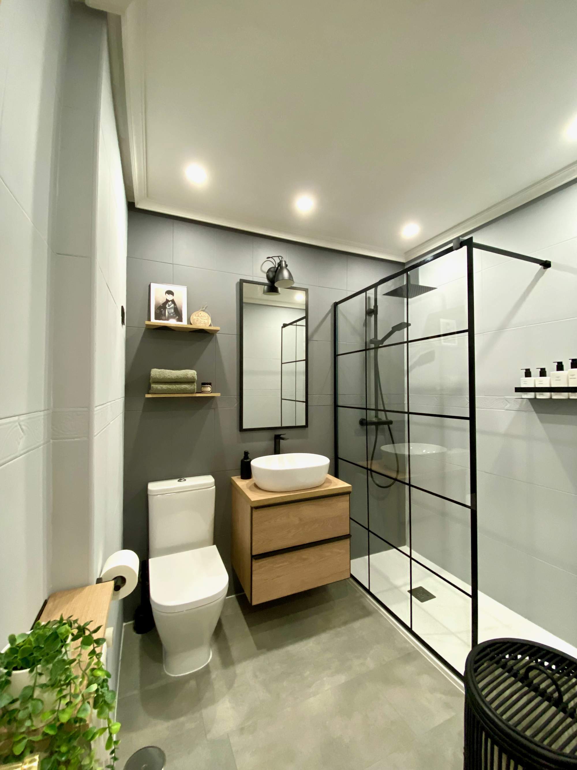 Baño con ducha con perfilería negra y revestimiento que imita el microcemento. 
