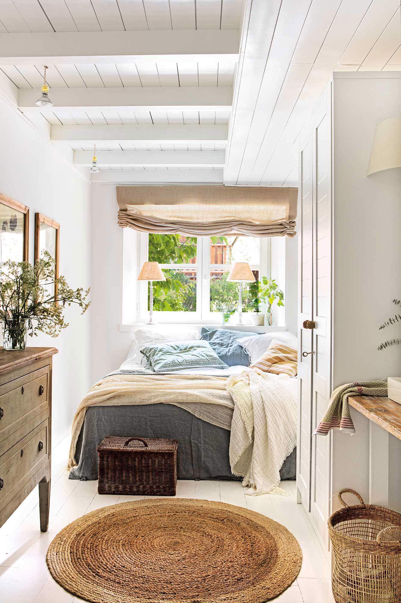Dormitorio con alfombra de yute y vigas blancas a la vista.