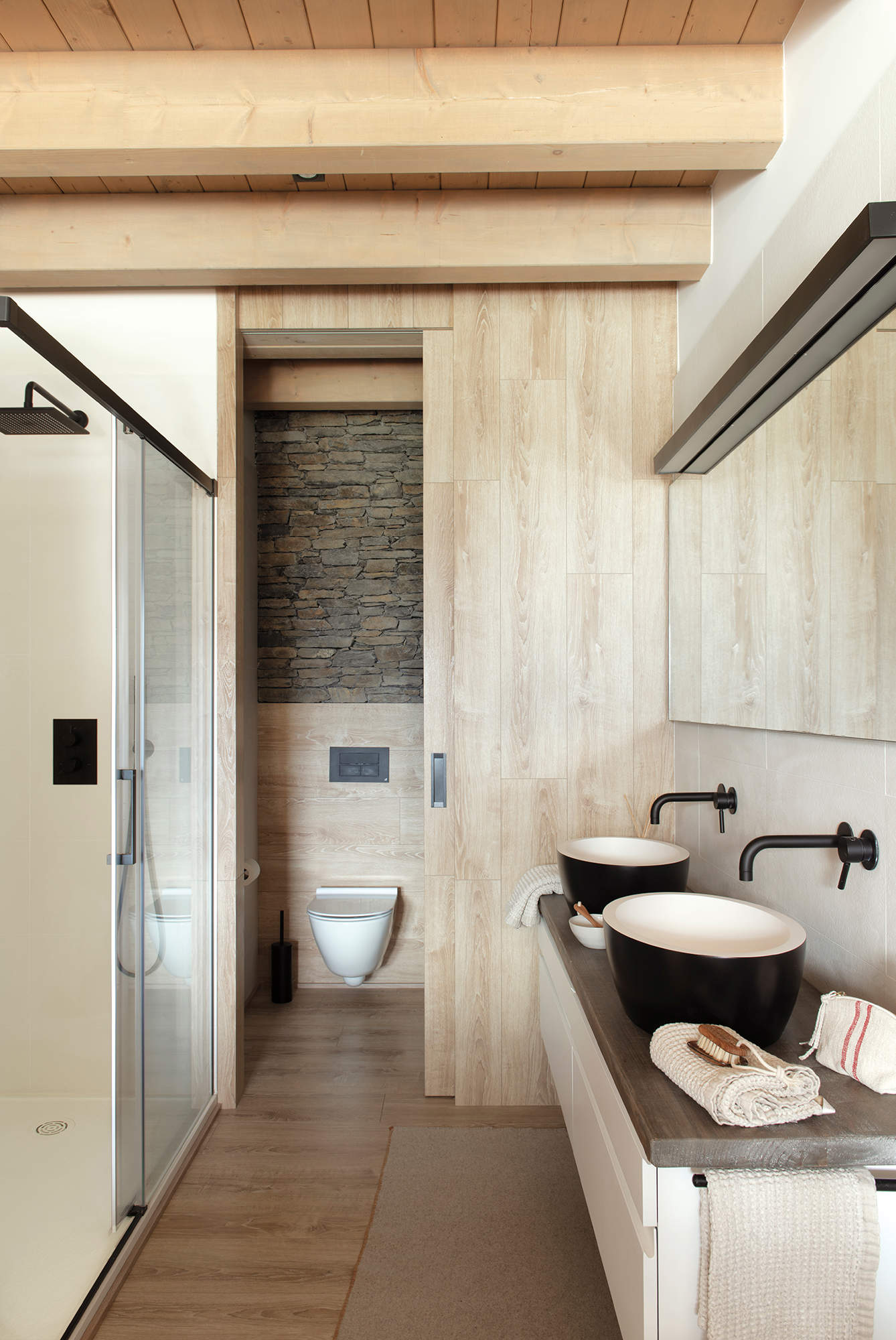 Baño con inodoro en cabina, decorado en tonos naturales y madera.