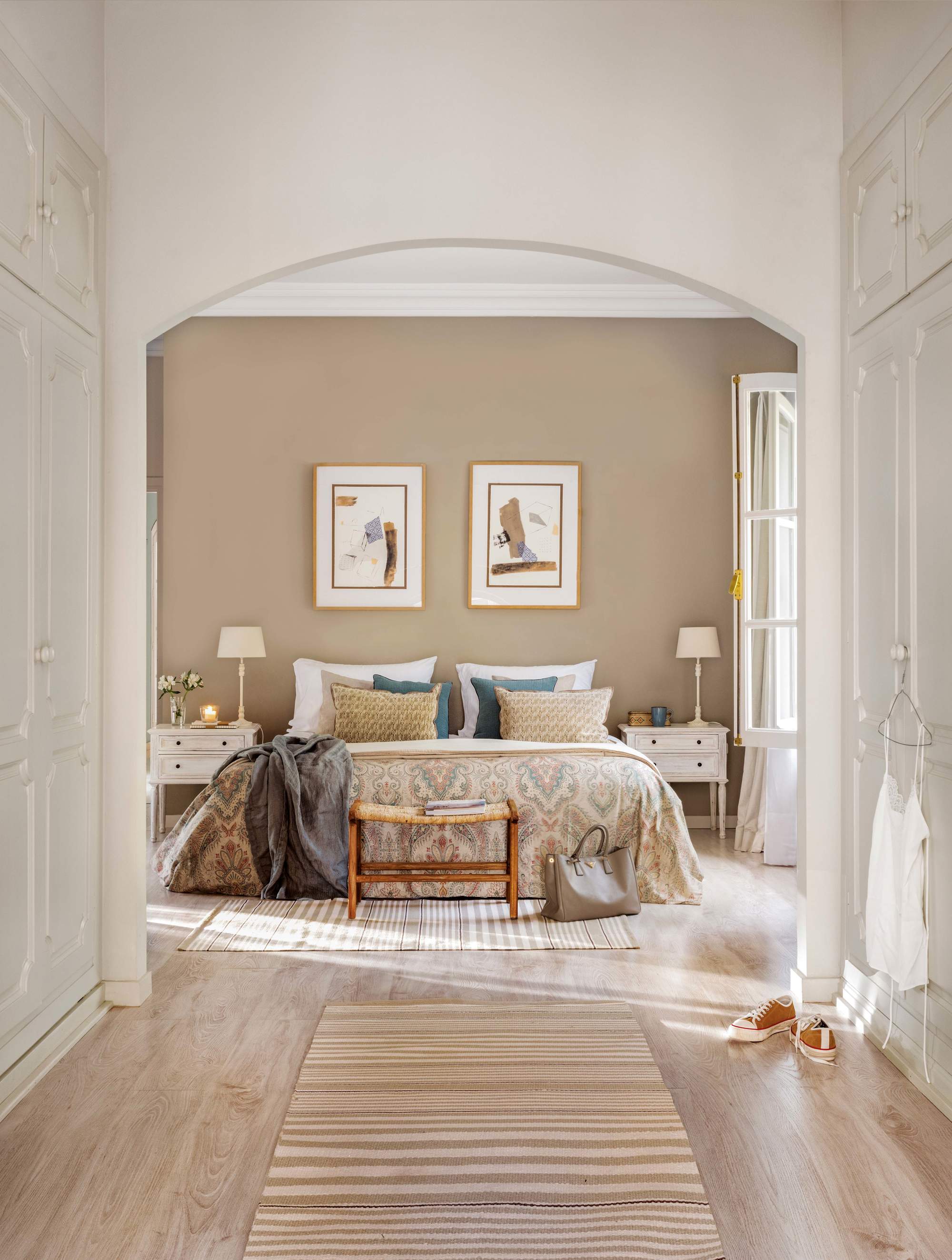 Dormitorio con pared de cabecero pintada de beige con cama, mesillas y cuadros