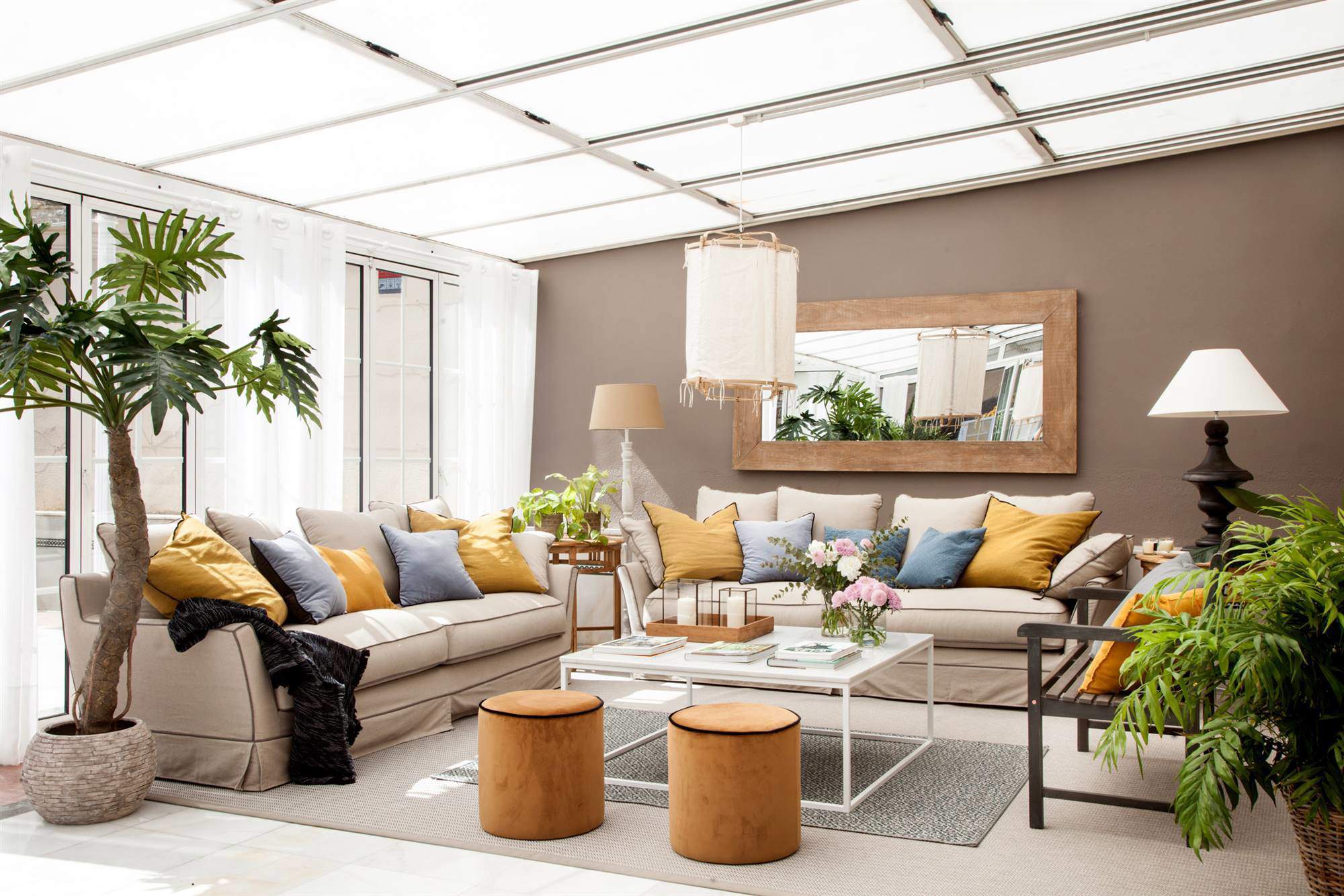 Salón acristalado con pared pintada de marrón, sofás, mesa de centro, pufs y planta XL