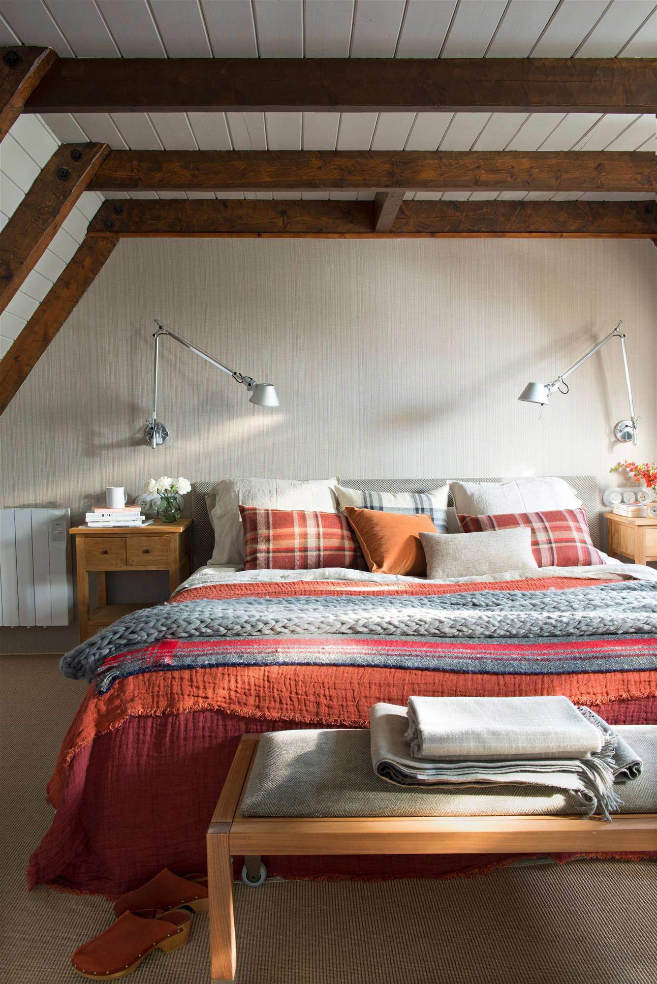 Dormitorio con vigas de madera a ala vista, y ropa de cama en granate y gris.